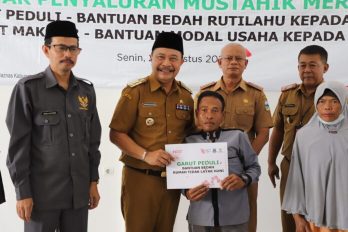 Pj. Bupati Garut, Barnas Adjidin, menyerahkan bantuan dari Baznas Kabupaten Garut, dalam acara Gebyar Penyaluran Bantuan Renovasi Rutilahu dan Garut Makmur, di Aula Kantor Baznas Kabupaten Garut, Jalan Pramuka, Kecamatan Garut Kota, Kabupaten Garut, Senin (26/8/2024).